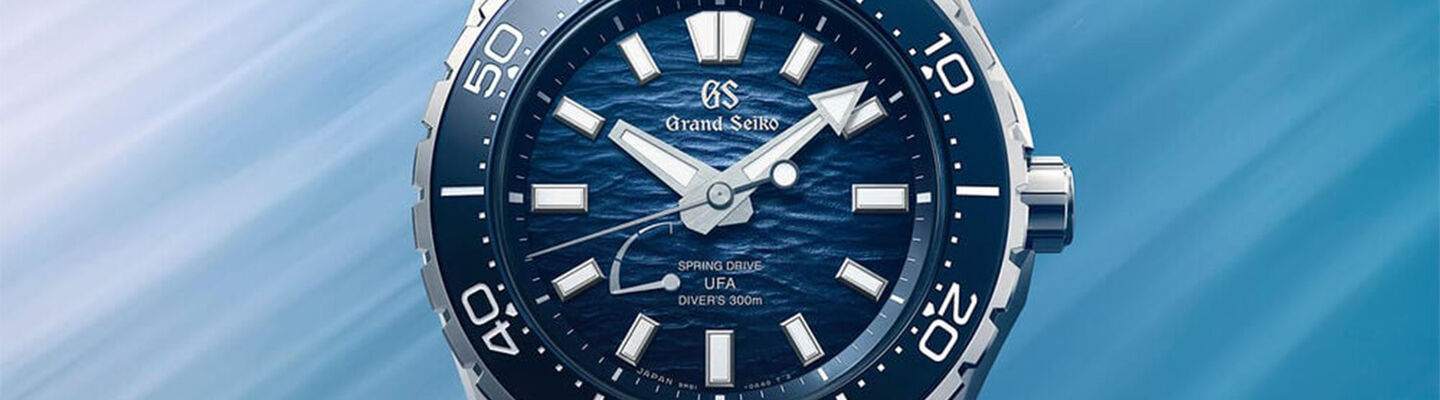 Close-up banner of a blue Grand Seiko Spring Drive UFA diver&rsquo;s watch with textured ocean-inspired dial, silver markers, and rotating bezel against a soft blue gradient background.